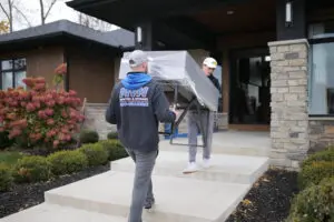 Two MVM Moving & Storage employees moving a desk wrapped in plastic into a house